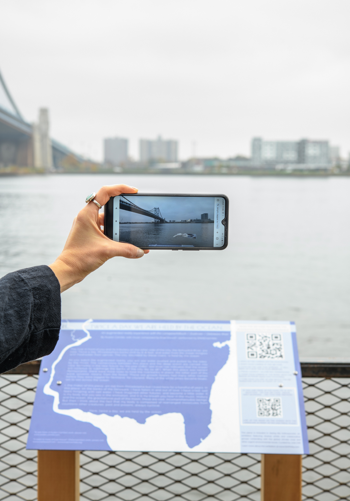 A hand holds up a smart phone to the Delaware River to experience an augmented reality artwork.