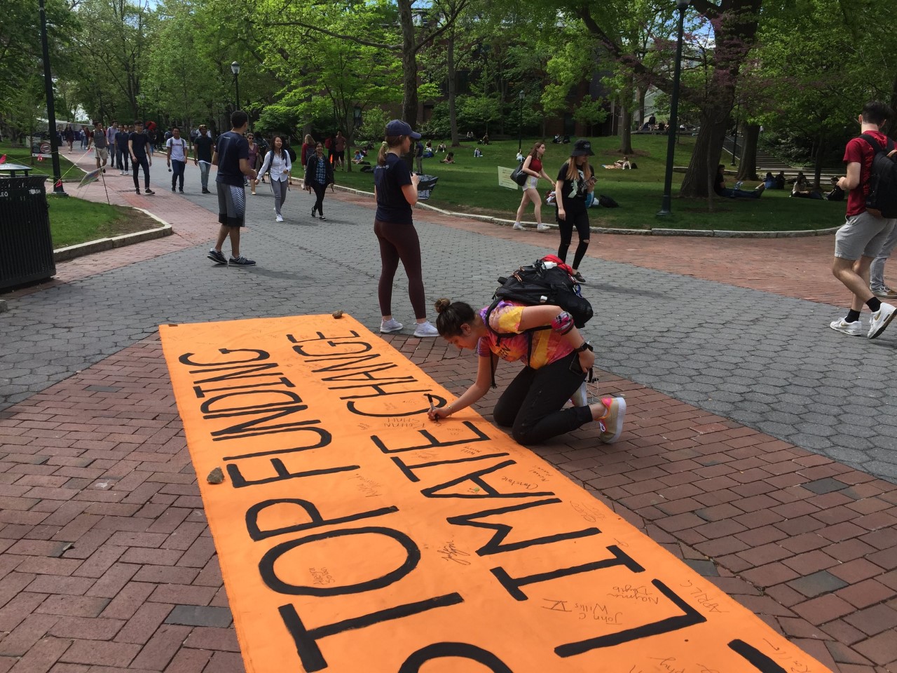 student adds signature to banner reading "Stop Funding Climate Change"