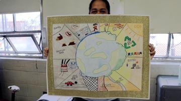 A woman holds up a student made poster with dos and donts for a healthy Earth.